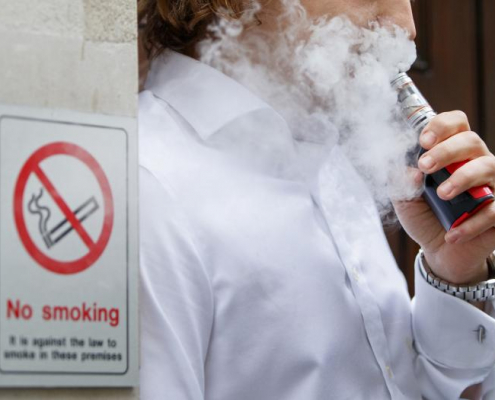 someone vaping in front of a no smoking sign