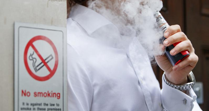 someone vaping in front of a no smoking sign