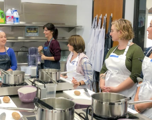 4 women at the UCLA test kitchen listening to a woman instructor teach a cooking class